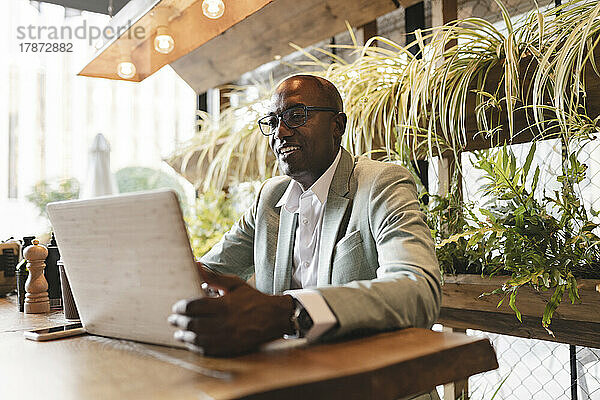 Lächelnder Geschäftsmann mit Laptop am Tisch im Café