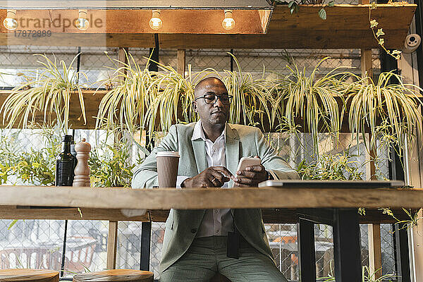 Reifer Geschäftsmann sitzt am Tisch im Café und nutzt sein Smartphone