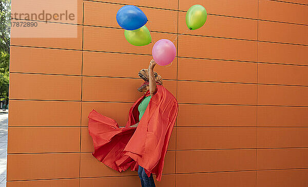 Frau mit Umhang hält bunte Luftballons vor der Wand