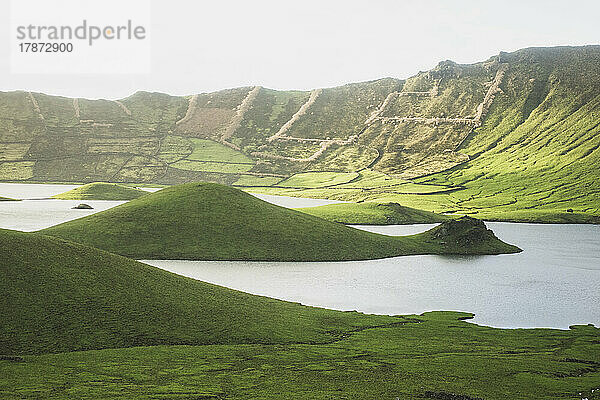 Idyllic view of lake amidst green hills on sunny day