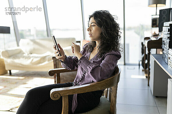Geschäftsfrau sitzt mit Smartphone auf Stuhl im Büro
