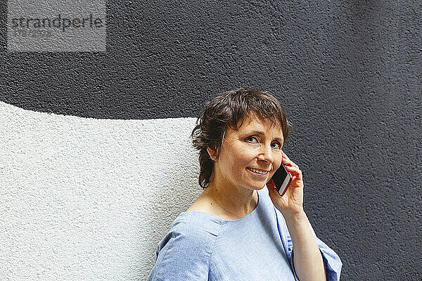 Reife Frau telefoniert an der Wand mit dem Handy