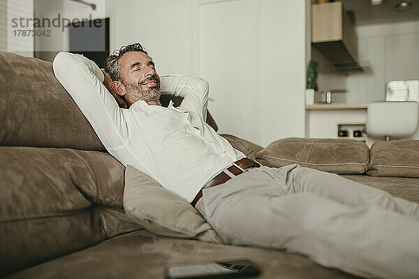 Lächelnder Geschäftsmann entspannt sich zu Hause auf dem Sofa