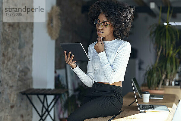 Nachdenkliche Geschäftsfrau blickt im Büro auf den Tablet-PC