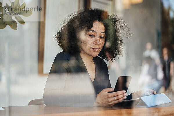 Frau benutzt Smartphone  gesehen durch Glas im Café