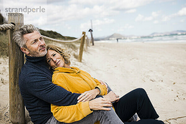 Lächelnde reife Frau mit Mann  der sich am Strand an eine Stange lehnt