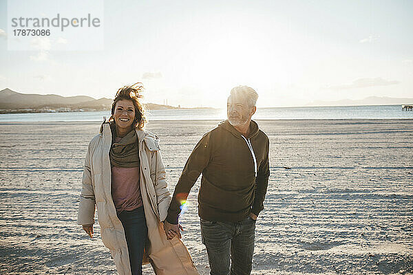 Glückliches älteres Paar  das an einem sonnigen Tag Händchen haltend am Strand spaziert