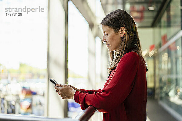 Geschäftsfrau benutzt Mobiltelefon am Geländer im Büroflur