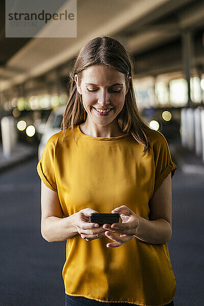 Lächelnde Geschäftsfrau benutzt Mobiltelefon auf Parkplatz