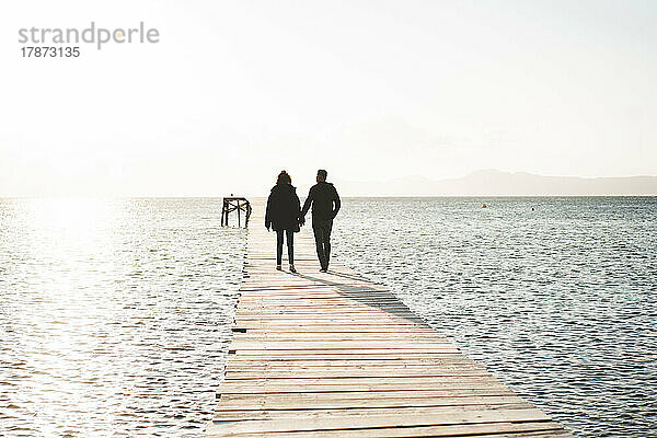 Couple holding hands walking on jetty over sea