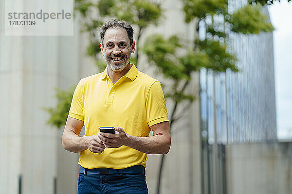 Glücklicher Mann mit Smartphone vor dem Gebäude
