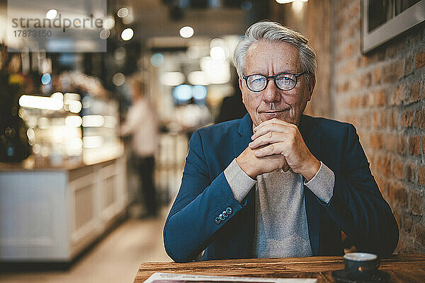 Selbstbewusster Geschäftsmann mit der Hand am Kinn im Café