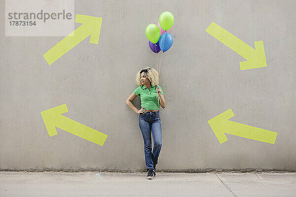 Frau steht mit der Hand auf der Hüfte und steht mit bunten Luftballons vor der Wand