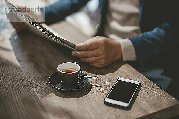 Geschäftsmann liest Zeitung bei Kaffee und Smartphone im Café
