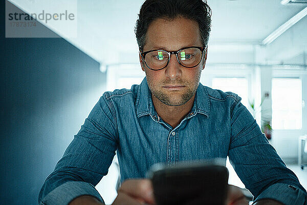 Businessman wearing eyeglasses using mobile phone in office
