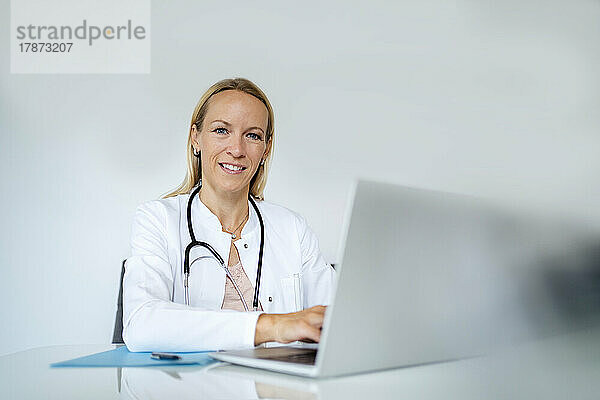 Porträt einer lächelnden Ärztin am Schreibtisch in der Arztpraxis