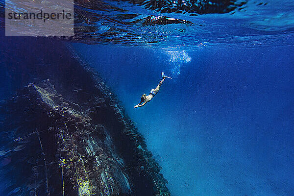 Woman diving underwater near shipwreck in sea