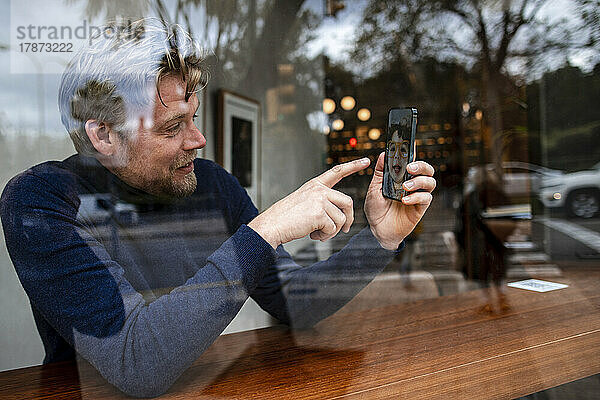 Geschäftsmann zeigt bei Videoanruf mit Tochter im Café auf Smartphone