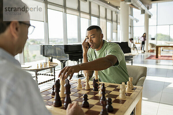 Geschäftsmann nimmt Schachfigur in die Hand und spielt mit Kollegen im Büro ein Brettspiel