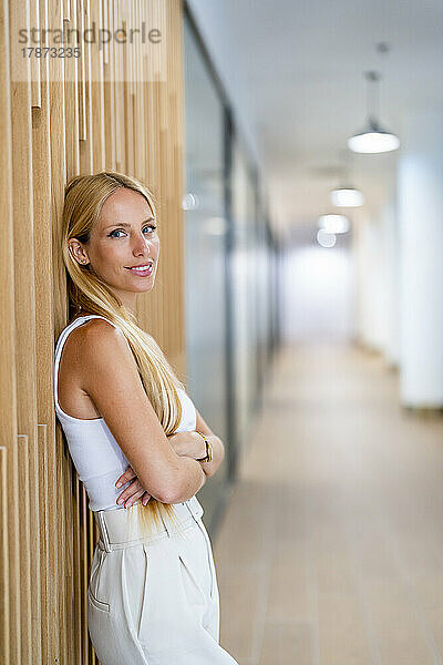 Lächelnde Geschäftsfrau lehnt im Büro an der Wand