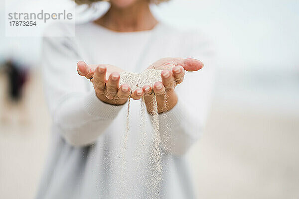 Hände einer reifen Frau  die Sand am Strand hält