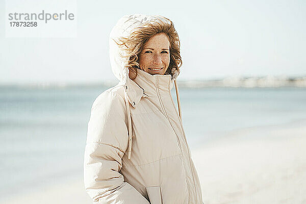 Lächelnde reife Frau  die am Strand steht