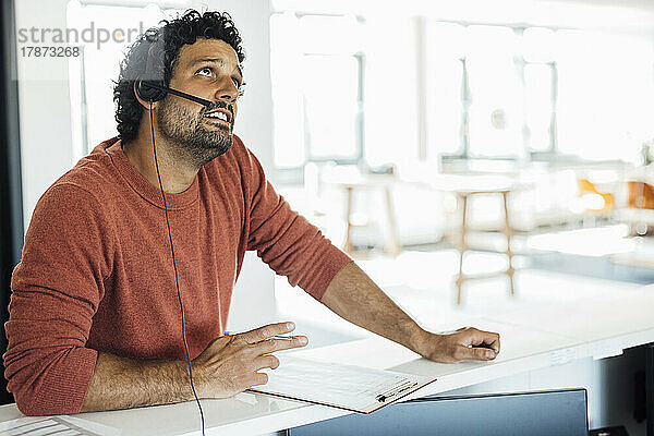 Nachdenklicher Geschäftsmann mit Headset sitzt am Arbeitsplatz