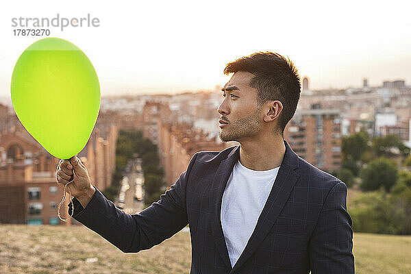 Nachdenklicher junger Geschäftsmann blickt auf grünen Ballon