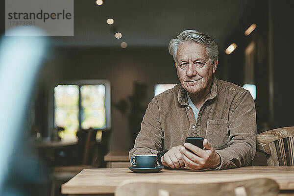 Lächelnder älterer Mann mit Mobiltelefon im Café