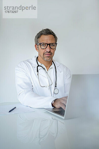 Portrait of mature doctor using laptop at desk in medical practice