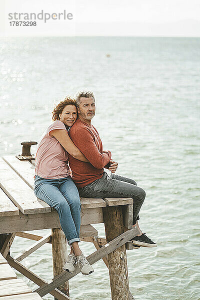 Smiling mature woman hugging man sitting on jetty