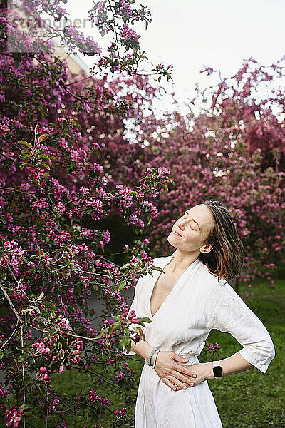 Lächelnde Frau mit geschlossenen Augen steht vor einem Apfelblütenbaum