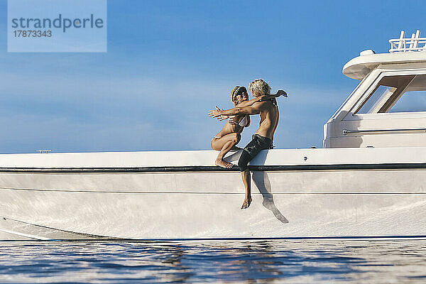 Lächelnde Frau umarmt ihren Freund  der auf dem Boot sitzt