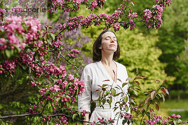 Lächelnde Frau mit geschlossenen Augen steht am Apfelblütenbaum
