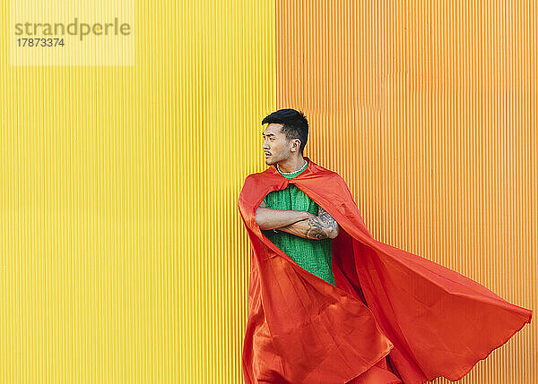 Nachdenklicher junger Mann mit rotem Superheldenumhang steht vor der Wand