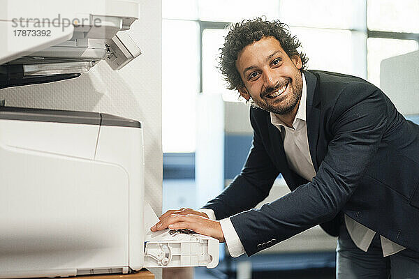 Lächelnder Geschäftsmann benutzt Computerdrucker im Büro