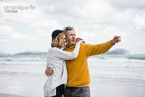 Glücklicher reifer Mann zeigt auf Frau  die am Strand steht