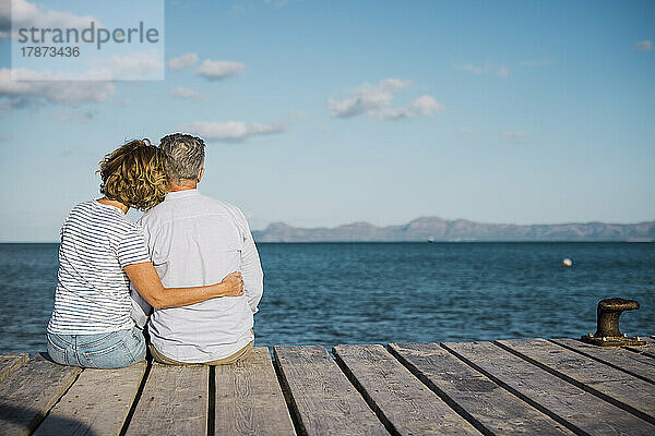 Älteres Paar verbringt Zeit miteinander  sitzt auf dem Steg und blickt aufs Meer