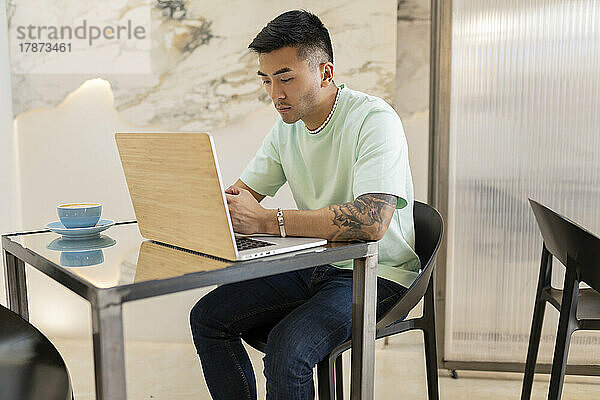 Junger Mann sitzt mit Laptop am Tisch im Café