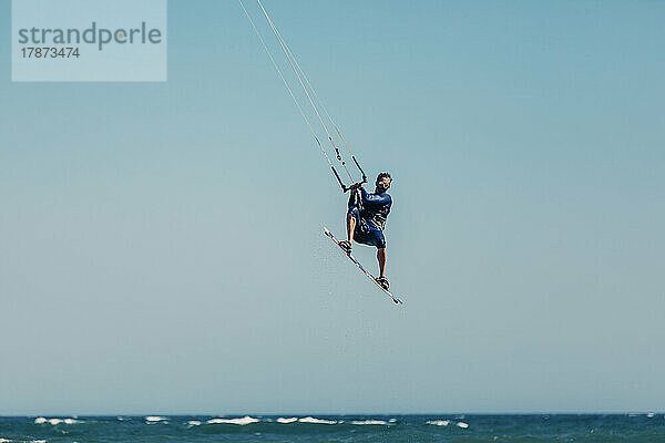 Reifer Mann beim Kitesurfen in der Luft über dem Meer an einem sonnigen Tag