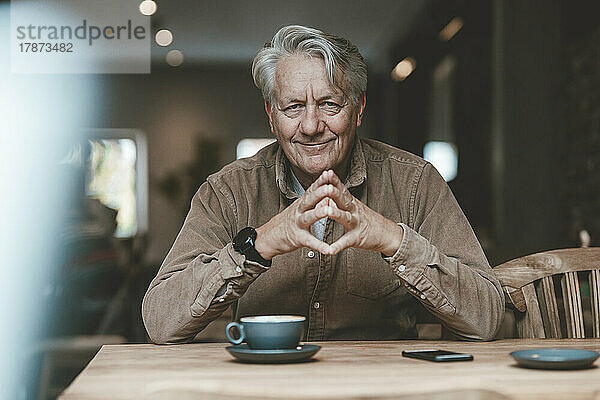 Lächelnder älterer Mann mit gefalteten Händen im Café