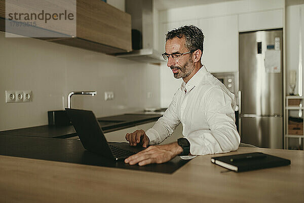 Geschäftsmann arbeitet am Laptop an der Küchentheke