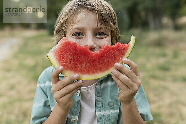 Junge hält sich eine Scheibe Wassermelone vors Gesicht