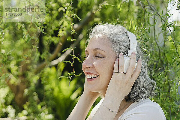Glückliche Frau genießt Musik über kabellose Kopfhörer im Park