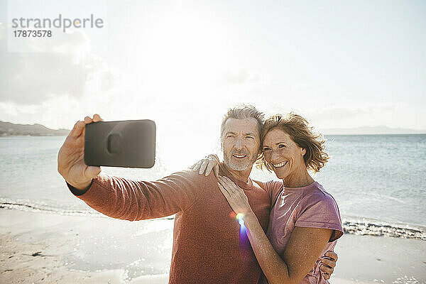 Glückliche reife Frau mit Mann  der am Strand ein Selfie per Smartphone macht