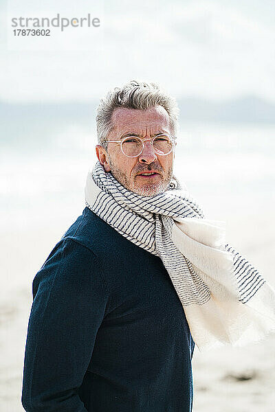 Reifer Mann mit Schal steht an einem sonnigen Tag am Strand