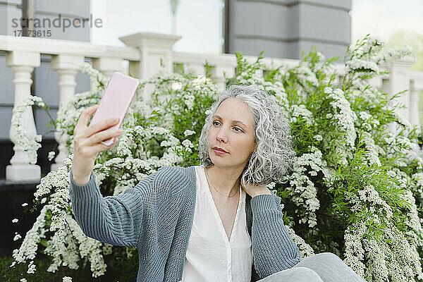 Frau macht Selfie mit Smartphone vor blühender Pflanze