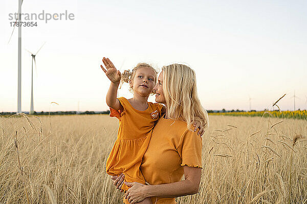 Lächelnde Frau mit Tochter gestikuliert im Weizenfeld