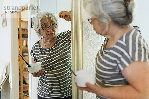 Ältere Frau untersucht weißes Haar und schaut zu Hause in den Spiegel