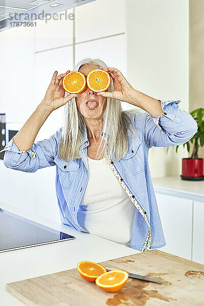 Fröhliche Frau bedeckt Augen mit Orangenscheiben in der Küche